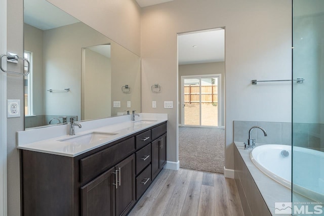 bathroom featuring vanity, tiled tub, and wood-type flooring