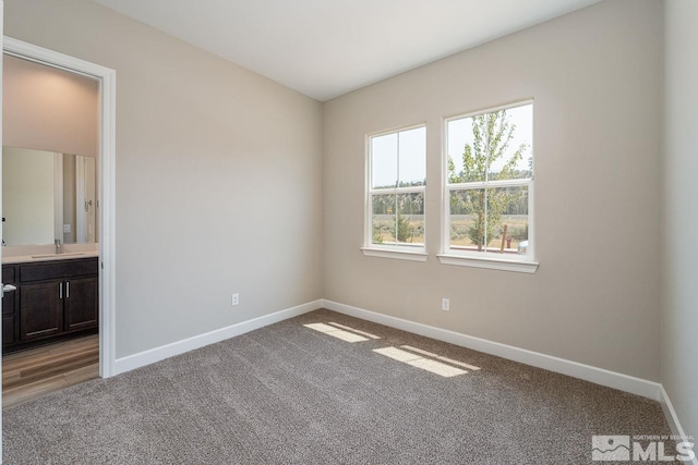 unfurnished bedroom featuring ensuite bathroom, carpet flooring, and sink