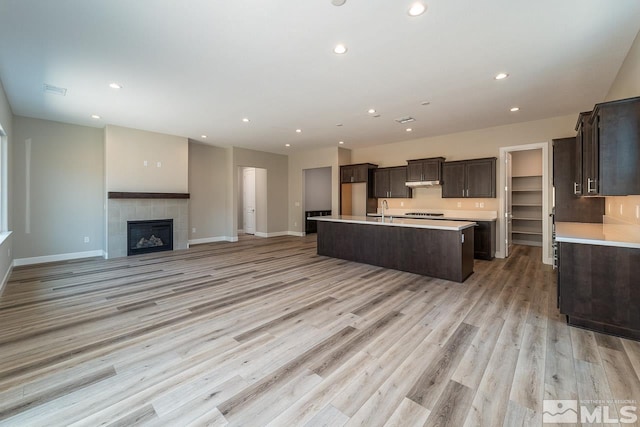 kitchen featuring a kitchen island with sink, sink, a tiled fireplace, and light hardwood / wood-style floors