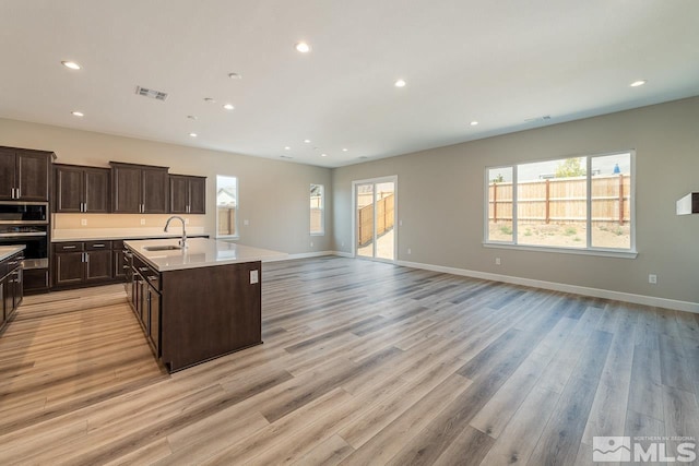 kitchen with sink, light wood-type flooring, an island with sink, and appliances with stainless steel finishes