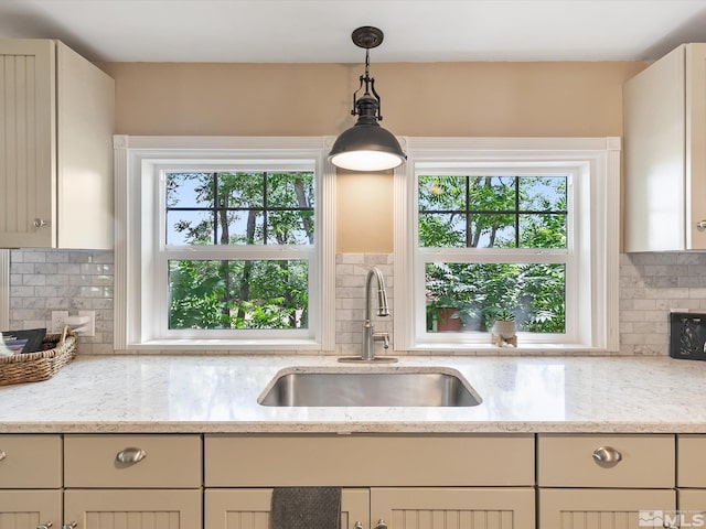 kitchen featuring tasteful backsplash, light stone countertops, sink, and pendant lighting