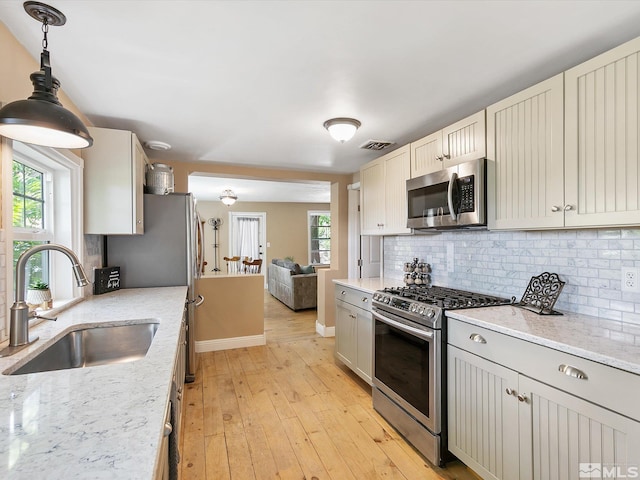 kitchen with sink, light stone counters, decorative light fixtures, a wealth of natural light, and stainless steel appliances