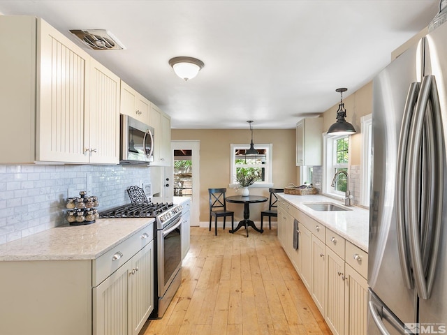 kitchen featuring decorative light fixtures, sink, decorative backsplash, light stone counters, and stainless steel appliances