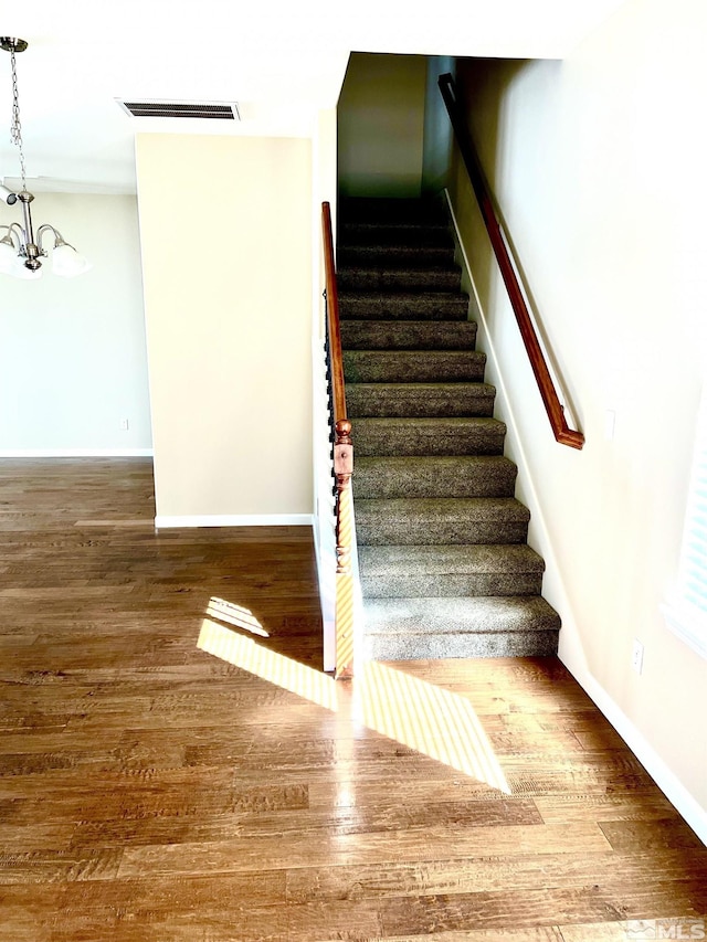 stairs with hardwood / wood-style floors and a chandelier