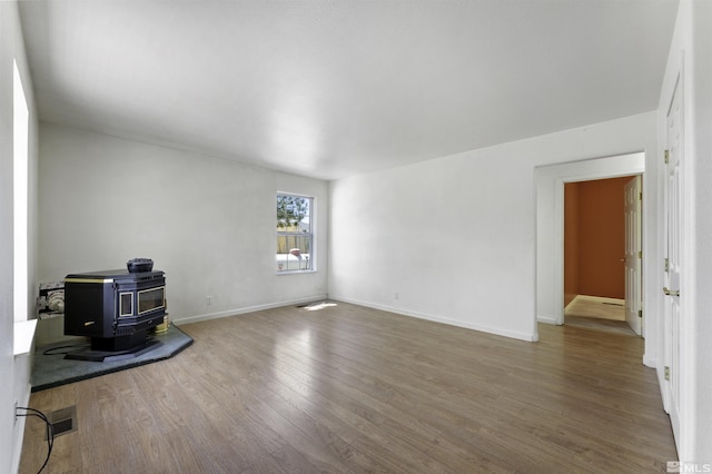 unfurnished room featuring visible vents, baseboards, wood finished floors, and a wood stove