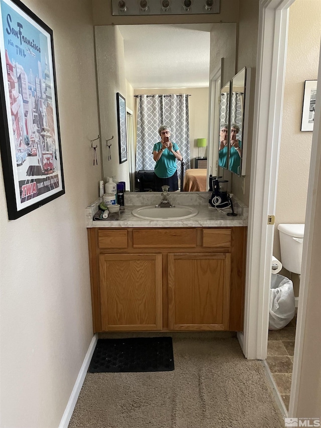 bathroom with toilet, baseboards, connected bathroom, and vanity