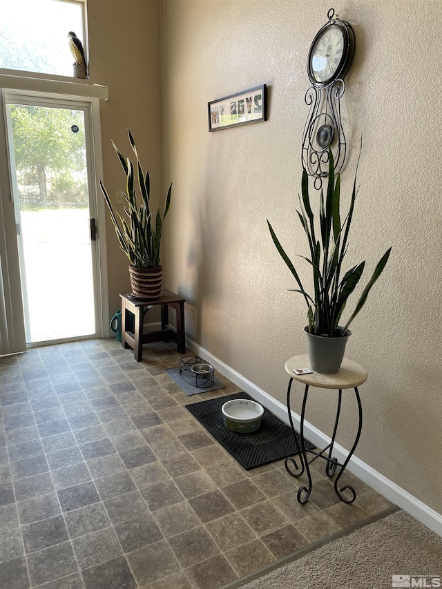 foyer entrance featuring a textured wall and baseboards