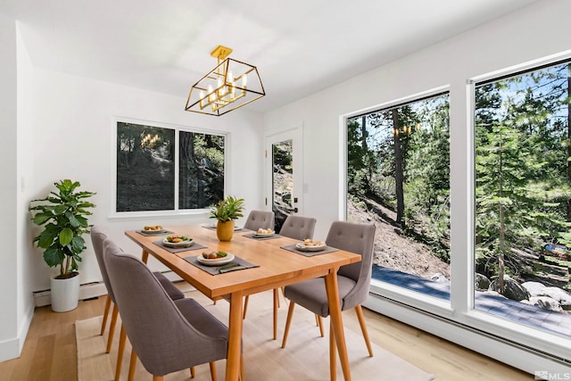 dining space with a baseboard heating unit, light hardwood / wood-style flooring, a chandelier, and plenty of natural light