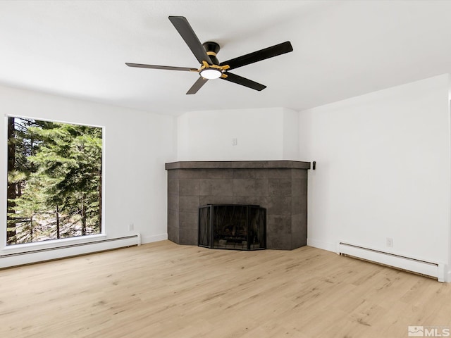 unfurnished living room featuring a baseboard heating unit, plenty of natural light, a fireplace, and light wood-type flooring