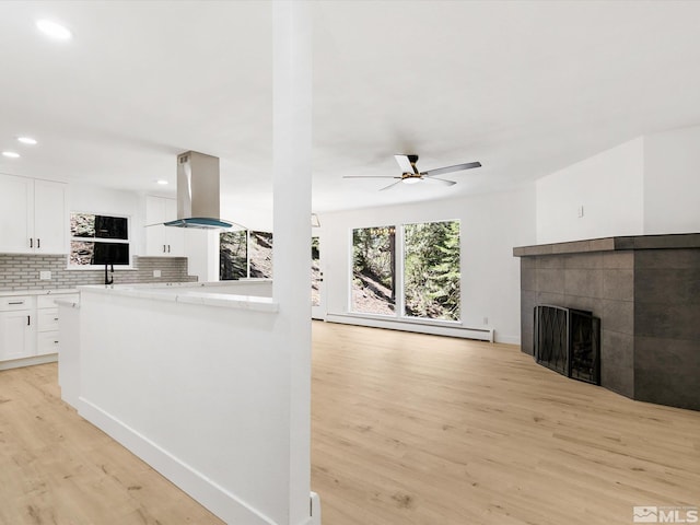 kitchen featuring island range hood, light wood-type flooring, a baseboard heating unit, white cabinets, and backsplash