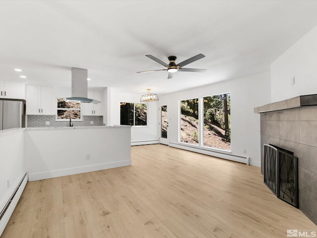 unfurnished living room featuring light hardwood / wood-style flooring, a tile fireplace, and baseboard heating