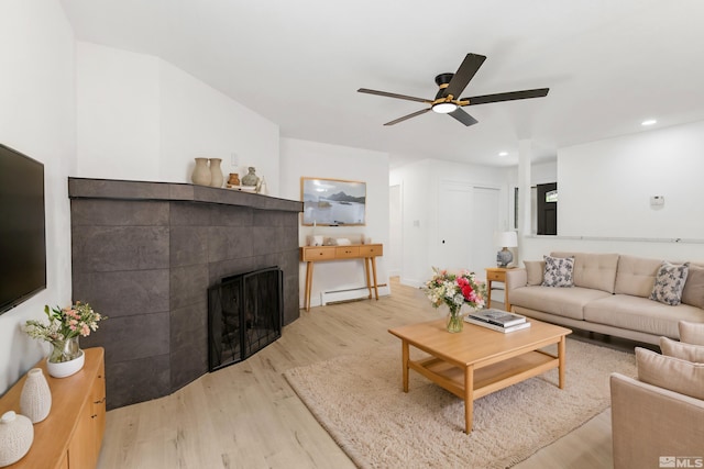 living room featuring ceiling fan, light wood-type flooring, a fireplace, and baseboard heating