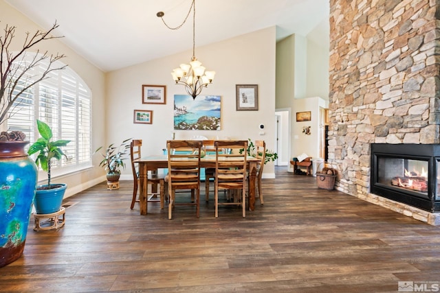 dining space featuring a chandelier, high vaulted ceiling, a stone fireplace, baseboards, and dark wood finished floors