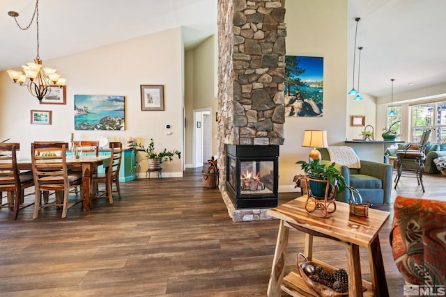 dining space with a chandelier, high vaulted ceiling, a stone fireplace, wood finished floors, and baseboards