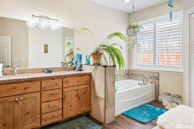 full bathroom with double vanity, a bath, a sink, and wood finished floors