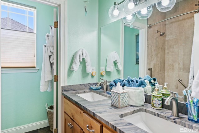 full bath with double vanity, a shower, a sink, and baseboards