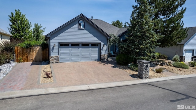 view of front of house with stone siding, decorative driveway, and fence