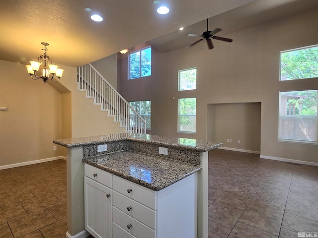 kitchen with white cabinetry, tile patterned floors, a high ceiling, ceiling fan with notable chandelier, and pendant lighting