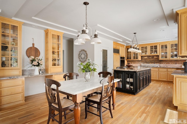 dining area with an inviting chandelier, a raised ceiling, and light hardwood / wood-style floors