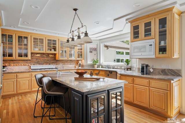 kitchen featuring white microwave, a kitchen island, decorative backsplash, light wood-type flooring, and light stone countertops