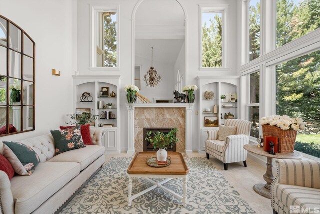 living room featuring a towering ceiling, a tiled fireplace, built in shelves, and a wealth of natural light