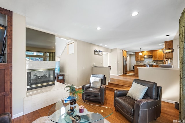 living room featuring sink, a tiled fireplace, and light hardwood / wood-style floors