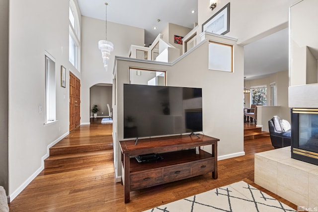 living room featuring an inviting chandelier, a towering ceiling, hardwood / wood-style floors, and a tile fireplace