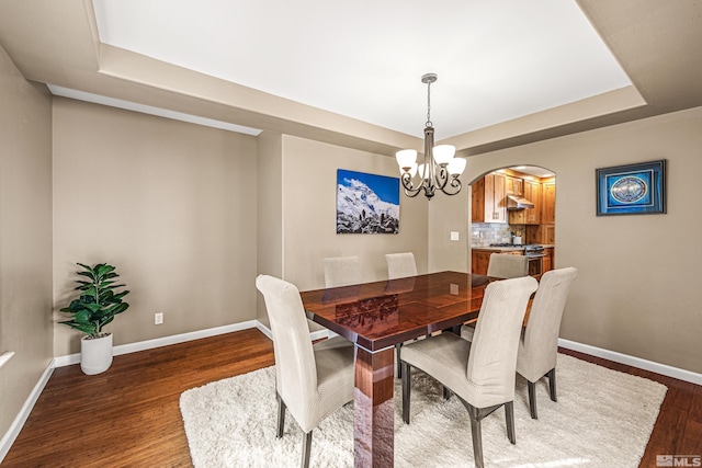 dining room with dark wood-type flooring, a notable chandelier, and a tray ceiling