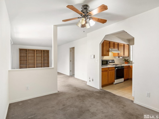 kitchen with under cabinet range hood, stainless steel microwave, light carpet, and white gas stove