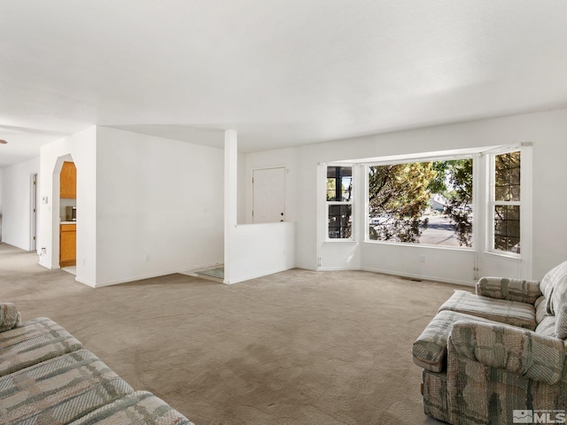 living room with baseboards, light carpet, and arched walkways