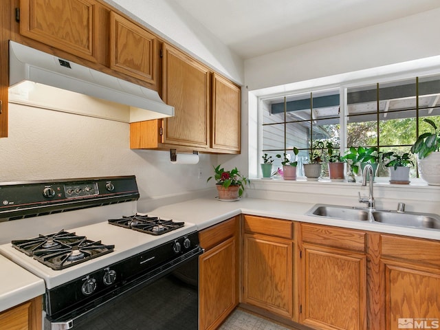 kitchen with under cabinet range hood, a sink, light countertops, and gas range oven