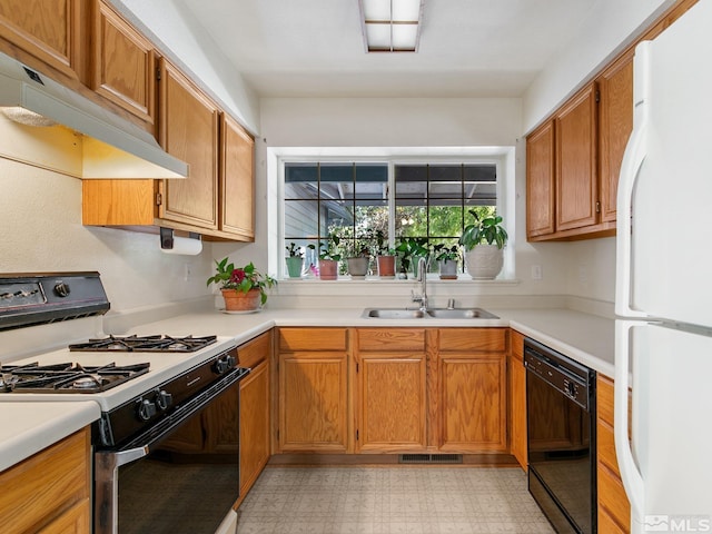 kitchen with under cabinet range hood, gas range, dishwasher, freestanding refrigerator, and a sink