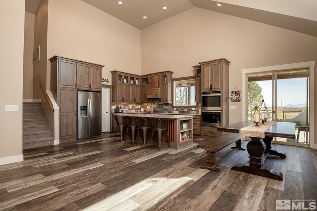 kitchen featuring appliances with stainless steel finishes, backsplash, dark hardwood / wood-style floors, a center island, and high vaulted ceiling