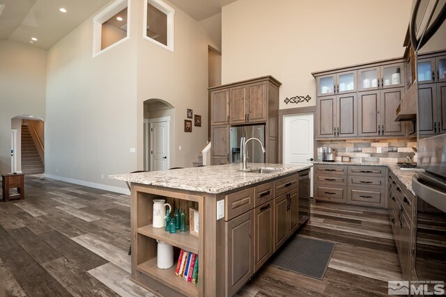 kitchen with a kitchen island with sink, dark hardwood / wood-style floors, light stone countertops, decorative backsplash, and a towering ceiling