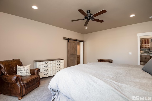 carpeted bedroom with ensuite bathroom, ceiling fan, and a barn door