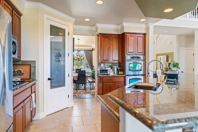 kitchen with a chandelier, dark stone counters, ornamental molding, light tile patterned floors, and stainless steel appliances