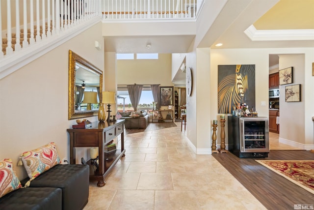 entryway with crown molding, bar, a towering ceiling, wine cooler, and light wood-type flooring