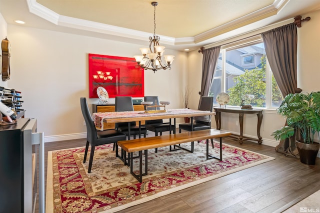 dining area with wood-type flooring, ornamental molding, an inviting chandelier, and a tray ceiling