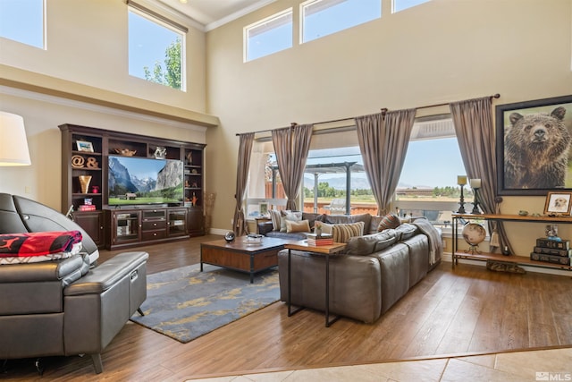 living room with crown molding, wood-type flooring, a wealth of natural light, and a towering ceiling