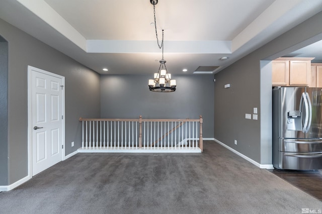 carpeted empty room featuring a notable chandelier and a tray ceiling