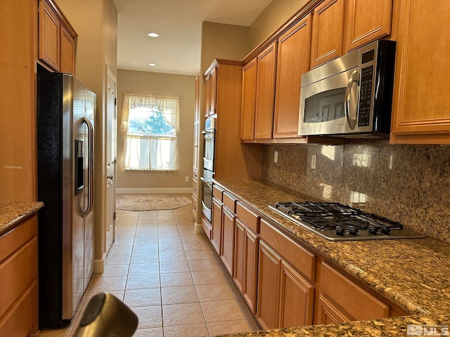 kitchen with decorative backsplash, stainless steel appliances, light tile patterned flooring, and dark stone countertops