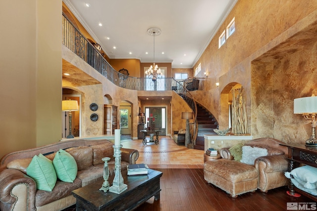 living room with hardwood / wood-style flooring, a notable chandelier, crown molding, and a high ceiling