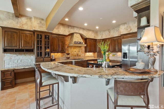 kitchen with tasteful backsplash, light tile patterned floors, stainless steel appliances, light stone countertops, and custom exhaust hood