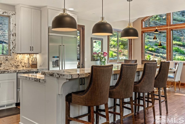 kitchen with white cabinetry, a center island, light stone countertops, and stainless steel built in fridge