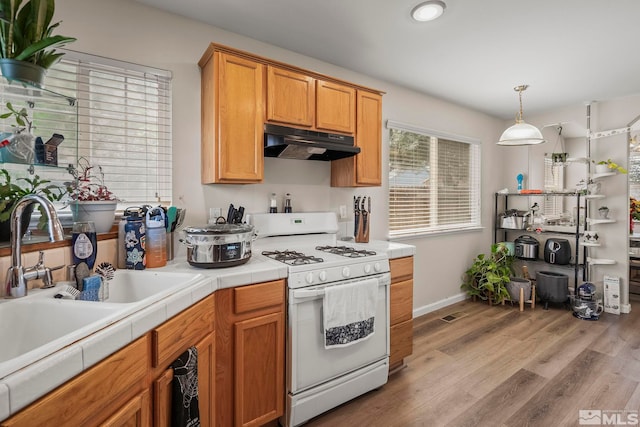 kitchen with white gas range, hanging light fixtures, light wood-type flooring, sink, and tile countertops