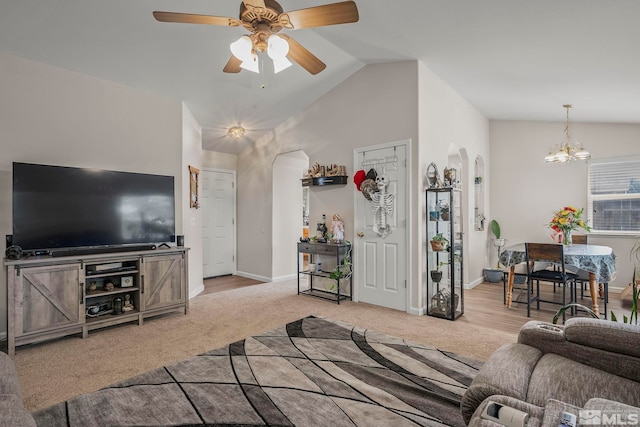 carpeted living room with ceiling fan with notable chandelier and vaulted ceiling