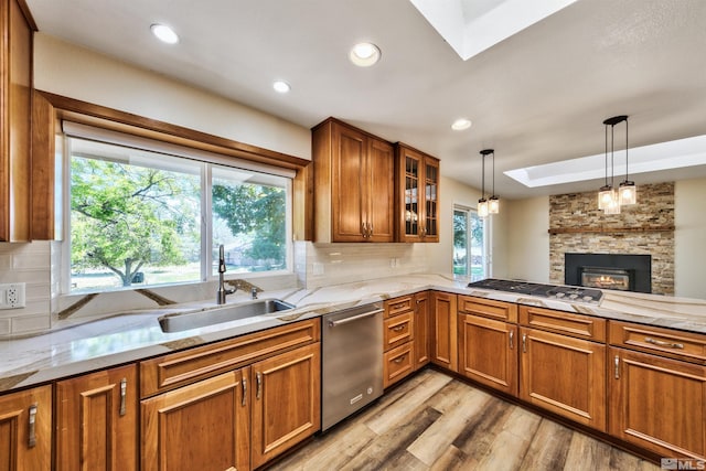 kitchen featuring tasteful backsplash, light wood-type flooring, a skylight, appliances with stainless steel finishes, and a stone fireplace