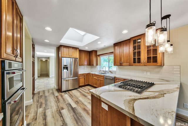 kitchen featuring appliances with stainless steel finishes, hanging light fixtures, light hardwood / wood-style floors, decorative backsplash, and a skylight