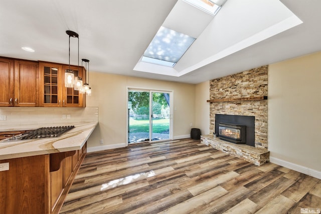 kitchen featuring a stone fireplace, pendant lighting, backsplash, lofted ceiling with skylight, and wood-type flooring