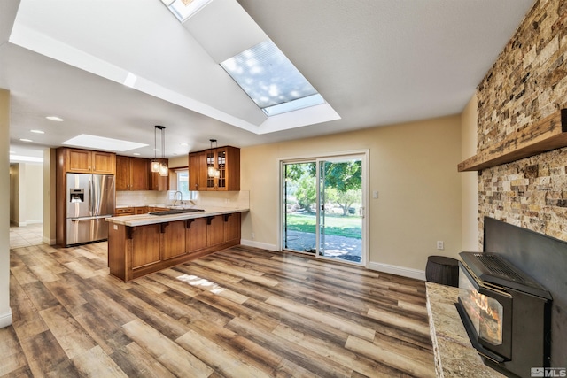 kitchen with a skylight, light wood-type flooring, stainless steel refrigerator with ice dispenser, and kitchen peninsula